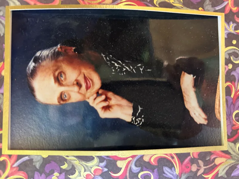 Portrait of Agnes Branch Pearlman, an older woman with striking blue eyes, wearing dark clothing with white patterned details, in a gold frame